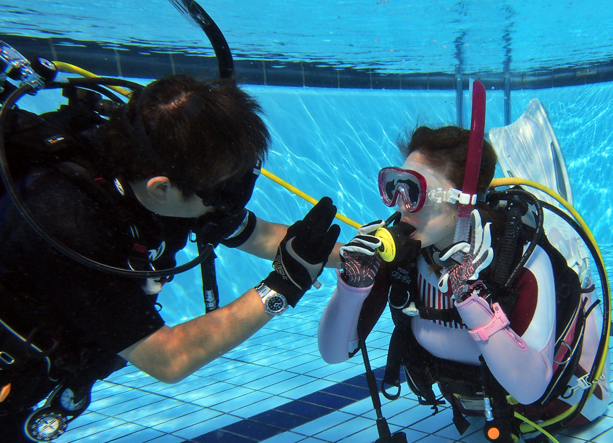ダイビング講習でインストラクターが初心者に近い距離で呼吸方法を教えている様子。少人数で安心して学べる環境